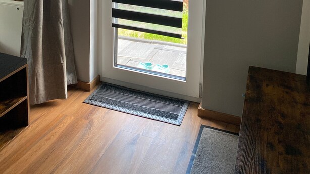 A door with horizontal blinds, a doormat, and a wooden floor. - Apartment 'Zum Kölpiensee' with Shared Terrace, Shared Garden and Wi-Fi (Peenemünde)