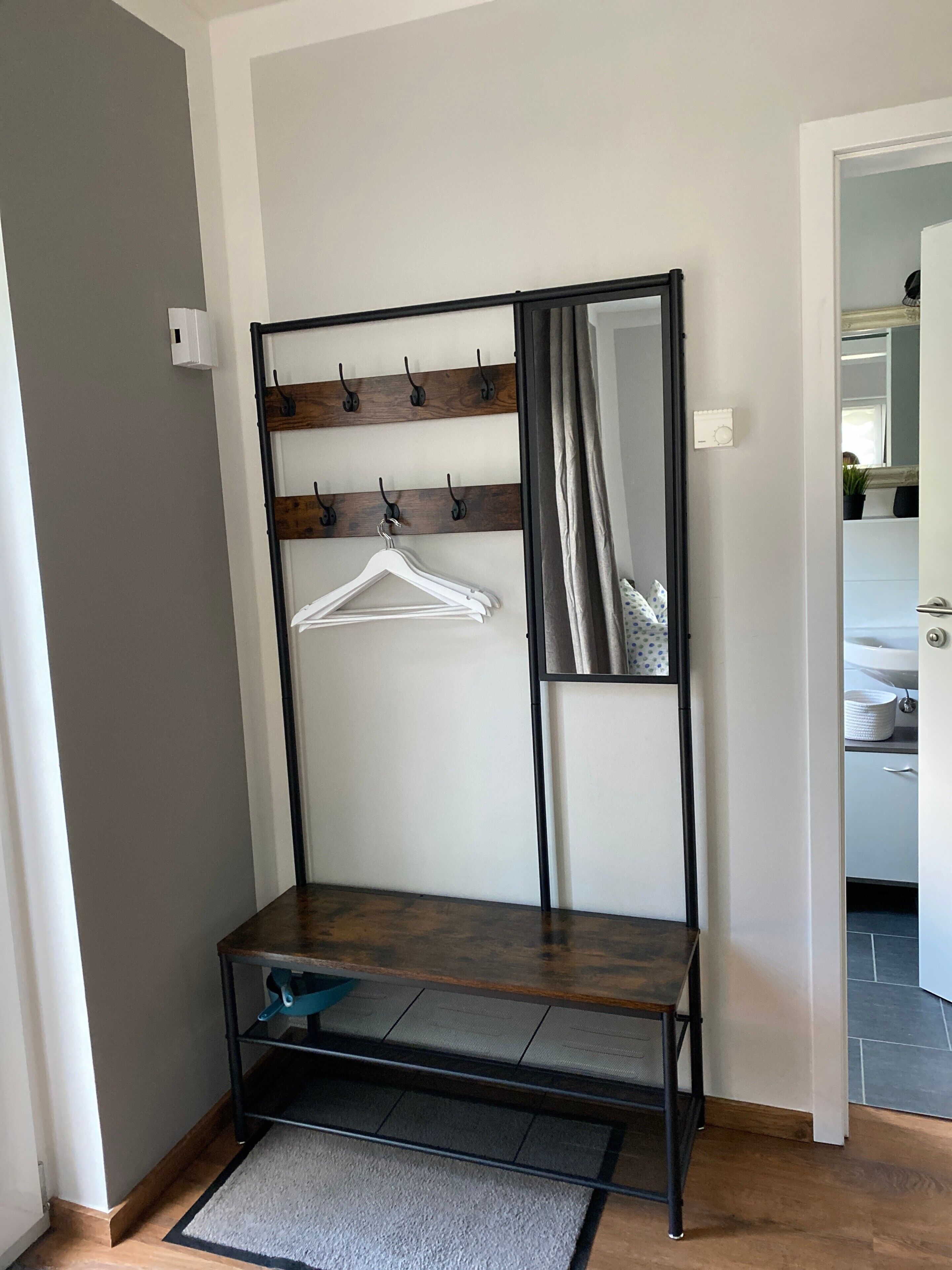 Een kamer met een bankje, een kapstok en een deur naar een badkamer.