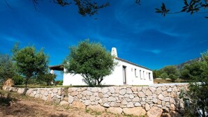 A white building with a stone wall in front, surrounded by trees and a clear blue sky. - Peaceful country house few minutes from the sea (Sardegna)