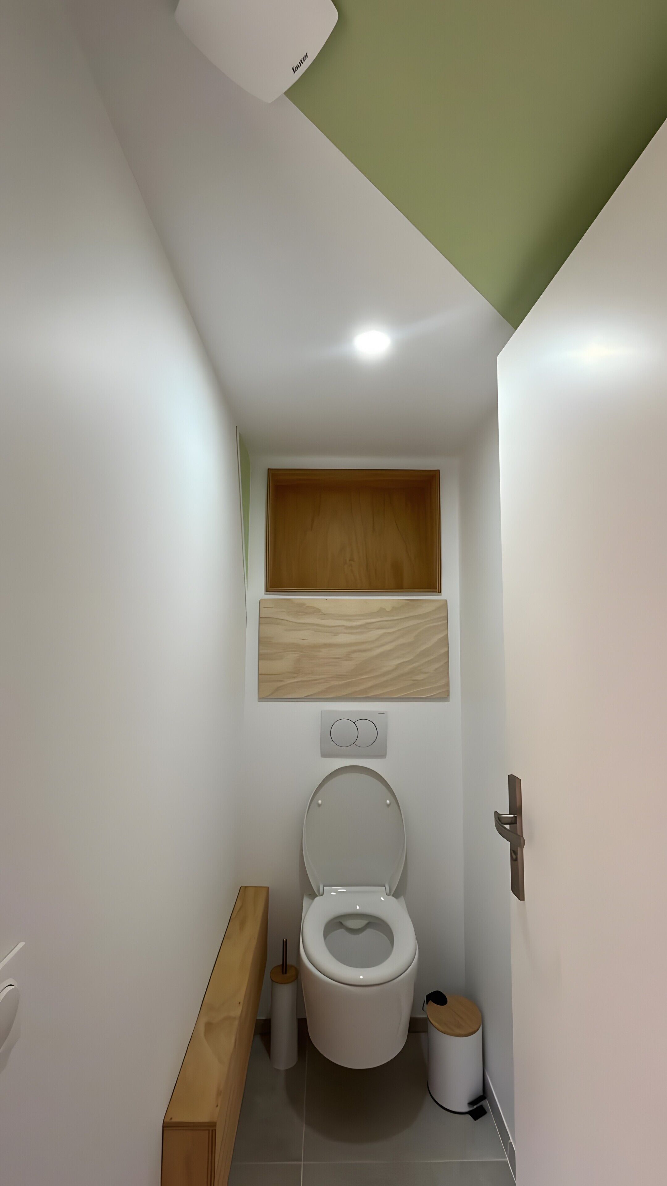 Une petite salle de bain comprenant des toilettes, une étagère en bois, un porte-rouleau de papier toilette et une poubelle.