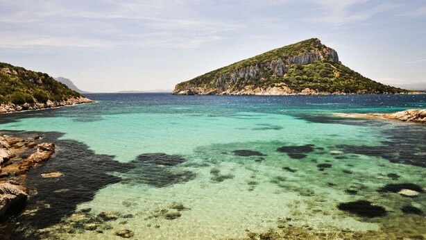 Un paysage côtier caractérisé par des eaux turquoise limpides, des rivages rocheux et une colline verdoyante qui se détache.