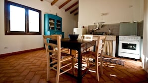 Une cuisine avec des poutres en bois, une table à manger avec des chaises, un buffet bleu et un poêle blanc.