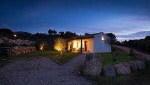 Une petite maison avec une allée en gravier, un mur en pierre et un arbre au premier plan.