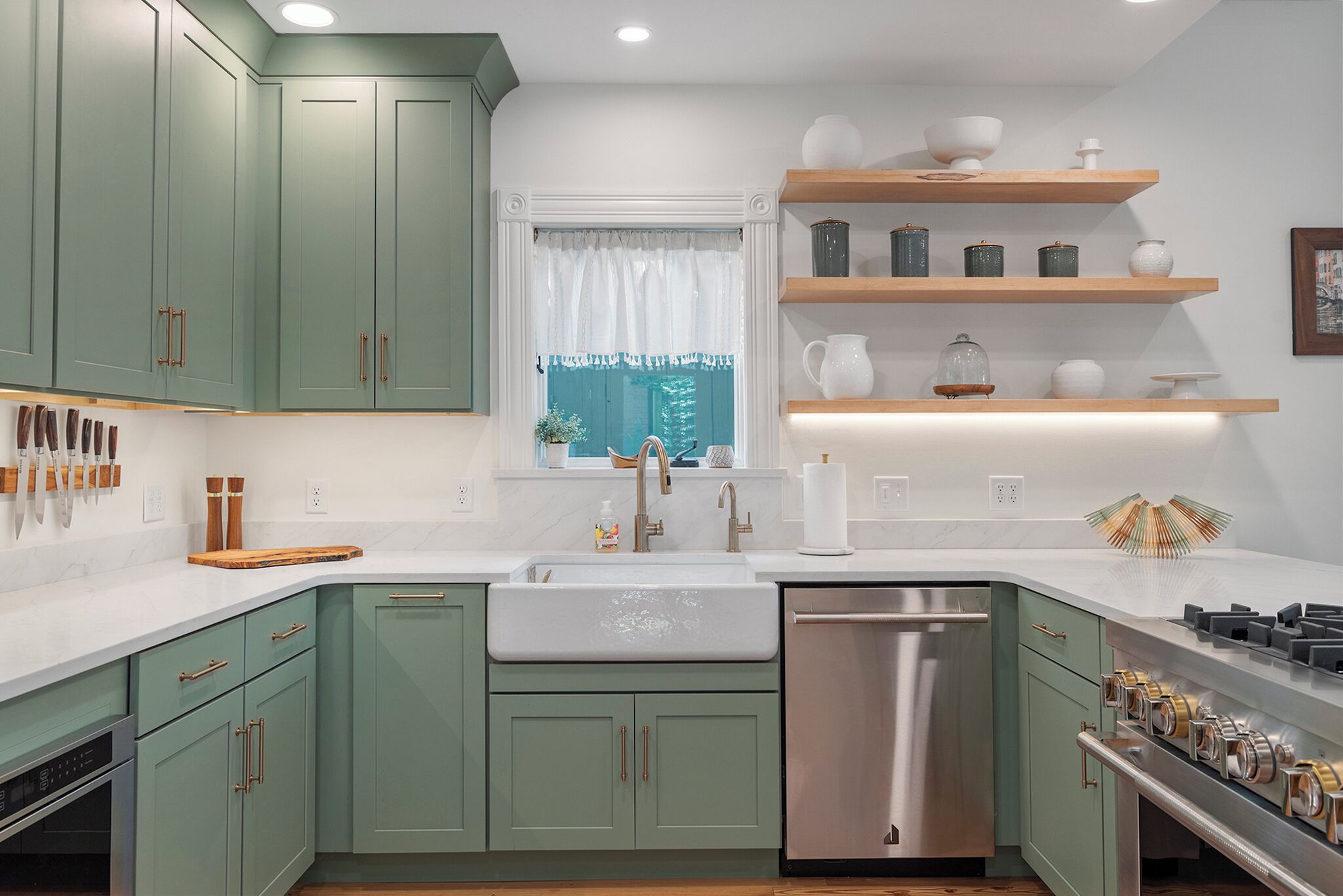 Cocina con armarios verdes, un lavamanos blanco y electrodomésticos de acero inoxidable.