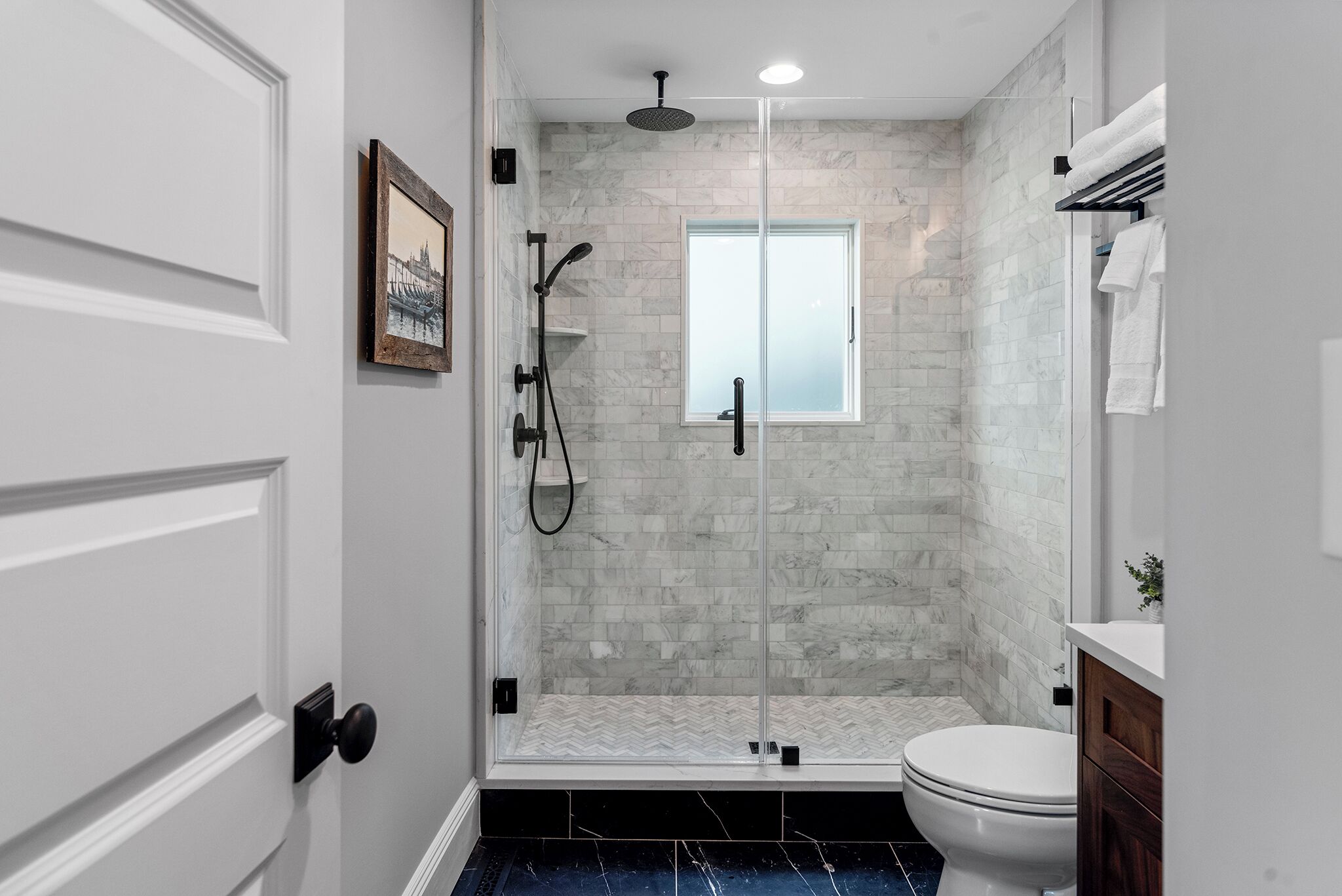 A modern bathroom with a glass-enclosed shower, a white toilet, and a marble-tiled shower wall.