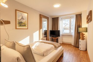 Habitación de hotel con cama, televisor, cómoda y ventana con cortinas.