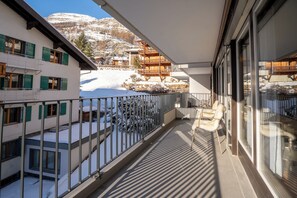 Un balcón con vistas a montañas nevadas y un edificio de madera al fondo.