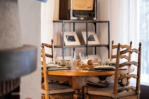 Mesa de madera con vajilla, tazas y jarra, rodeada de sillas tapizadas.