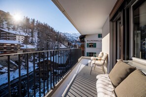Un balcón con vistas a un paisaje montañoso nevado, un sofá y un letrero que dice "ALPENBLICK".