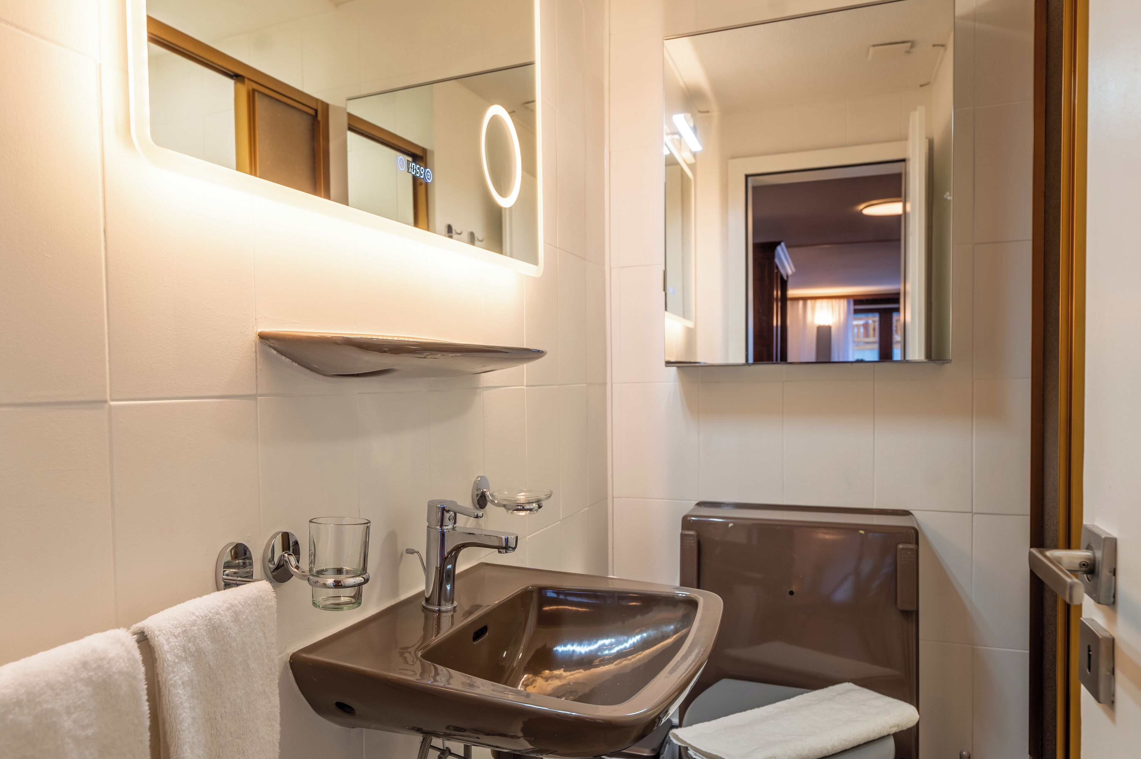 Une salle de bain avec un grand miroir, un lavabo avec un verre et un porte-serviettes.