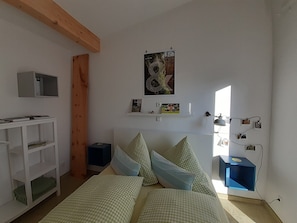 Un dormitorio con cama, escritorio, estante con fotografías y ventana.