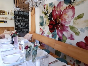 A dining area with a table set for a meal, a floral painting on the wall, and a chalkboard with text. - Room 'No. 2' with Shared Terrace, Shared Garden and Wi-Fi (Bad Urach)