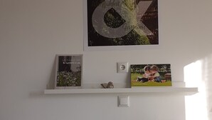 A wall with a framed poster, a small shelf with books, and a white switchboard. - Apartment 'No. 3' with Shared Terrace, Shared Garden and Wi-Fi (Bad Urach)