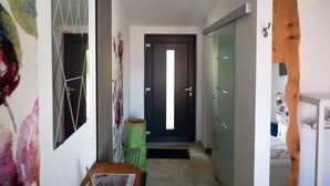 A hallway with a wooden ceiling, a door at the end, a green chair, and a bed with a white headboard. - Apartment 'No. 3' with Shared Terrace, Shared Garden and Wi-Fi (Bad Urach)