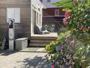 A wooden deck with a seating area, a charging station, and a garden with pink flowers. - Tiny Home 'Friedlinde' with Shared Terrace, Shared Garden and Wi-Fi (Bad Urach)
