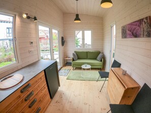 Ein gemütlicher Raum mit Holzboden, einem grünen Sofa, einem kleinen Tisch und einer Küchenzeile mit Spüle und Schränken.