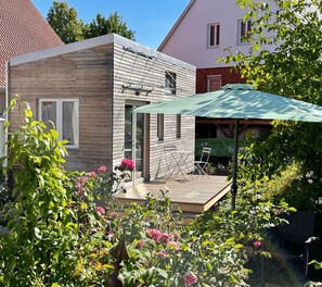 Ein modernes Haus mit einer Holzterrasse, einem grünen Sonnenschirm und blühenden Blumen.