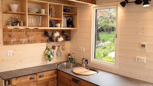 A kitchen with wooden cabinets, a window with a view, a sink, and various kitchen utensils. - Tiny Home 'Friedlinde' with Shared Terrace, Shared Garden and Wi-Fi (Bad Urach)