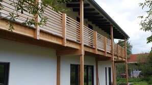 A modern building with a wooden balcony, large windows, and a covered outdoor area. - Tiny Home 'Friedlinde' with Shared Terrace, Shared Garden and Wi-Fi (Bad Urach)