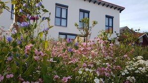 A white building with multiple windows and a garden with various flowers. - Room 'No. 4' with Shared Terrace, Communal Garden and Wi-Fi (Bad Urach)