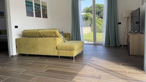 A modern living room with a yellow sofa, a wooden floor, and a sliding glass door leading to a garden.