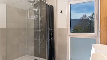 Ein modernes Badezimmer mit einer Duschkabine, einem Fenster mit Blick auf Bäume und einer weißen Badewanne.