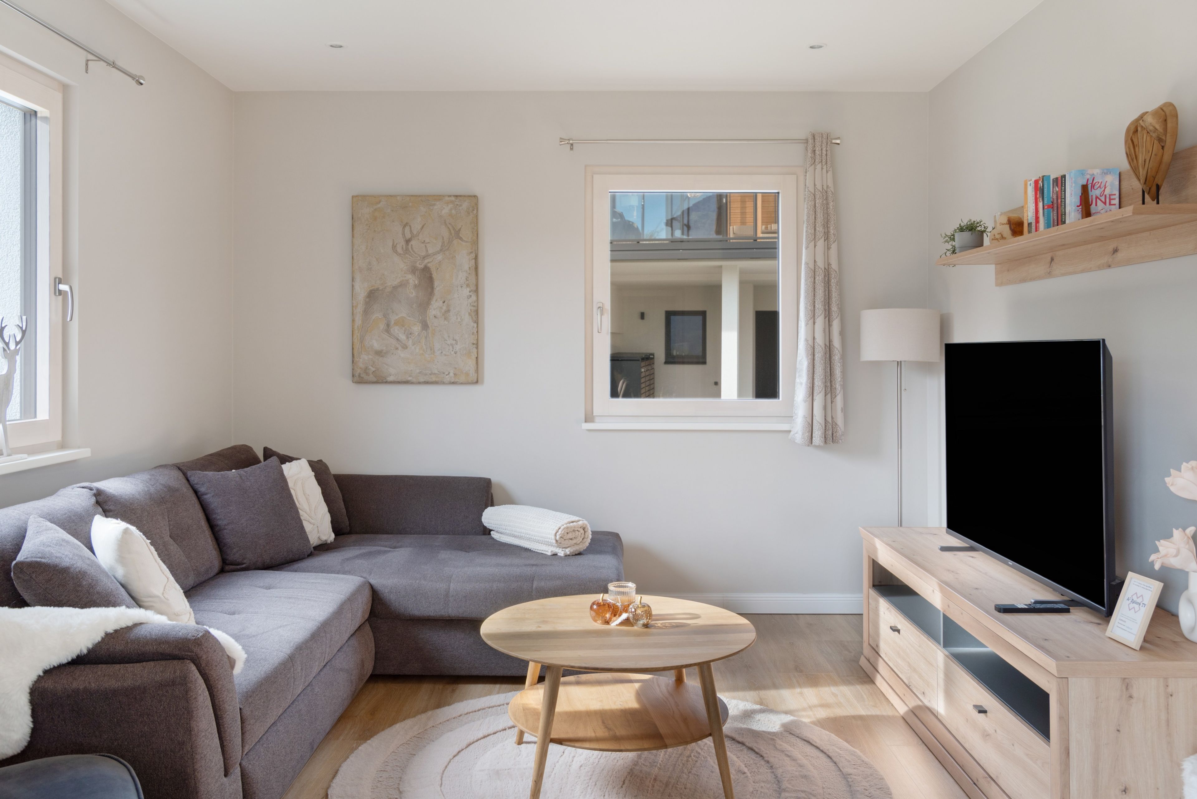 A modern living room with a grey sofa, a round wooden coffee table, a flat-screen TV, and a bookshelf with books and decorative items.
