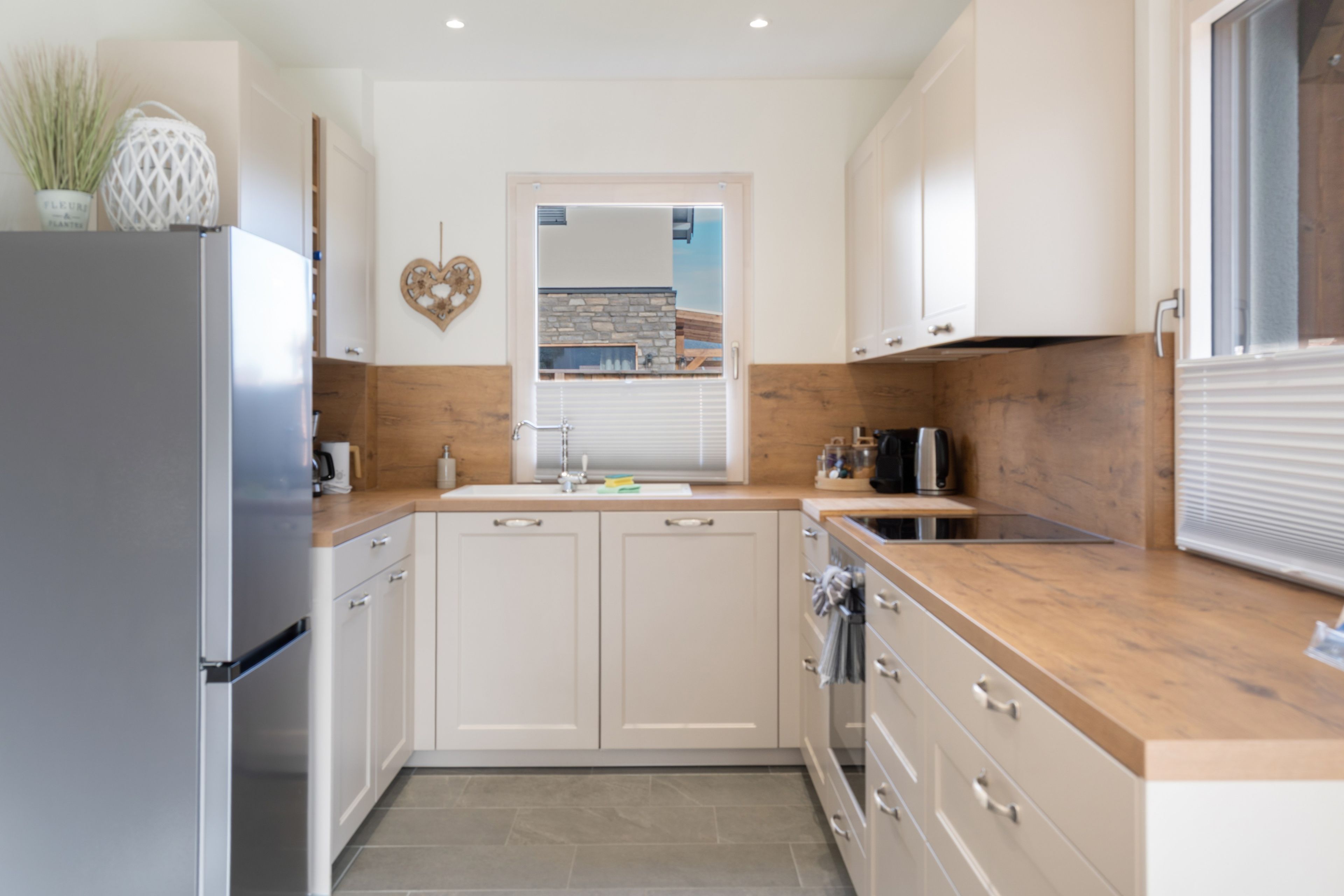 A modern kitchen with white cabinets, a stainless steel refrigerator, and a wooden countertop.