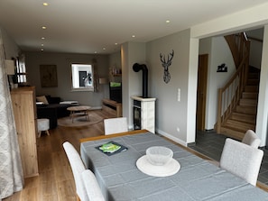 A modern living room with a dining area, wooden flooring, a fireplace, and a staircase.