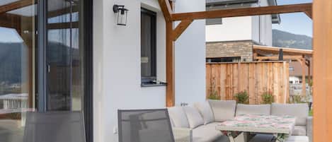 A covered outdoor seating area with a table and chairs, a screen door, and a wooden pergola structure.