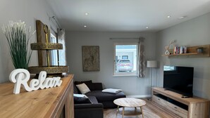 A modern living room with a sofa, a TV, a wooden coffee table, and a decorative bowl. - Holiday Home 'Almrausch' with Lake View, Private Terrace and Wi-Fi (Bodensdorf)