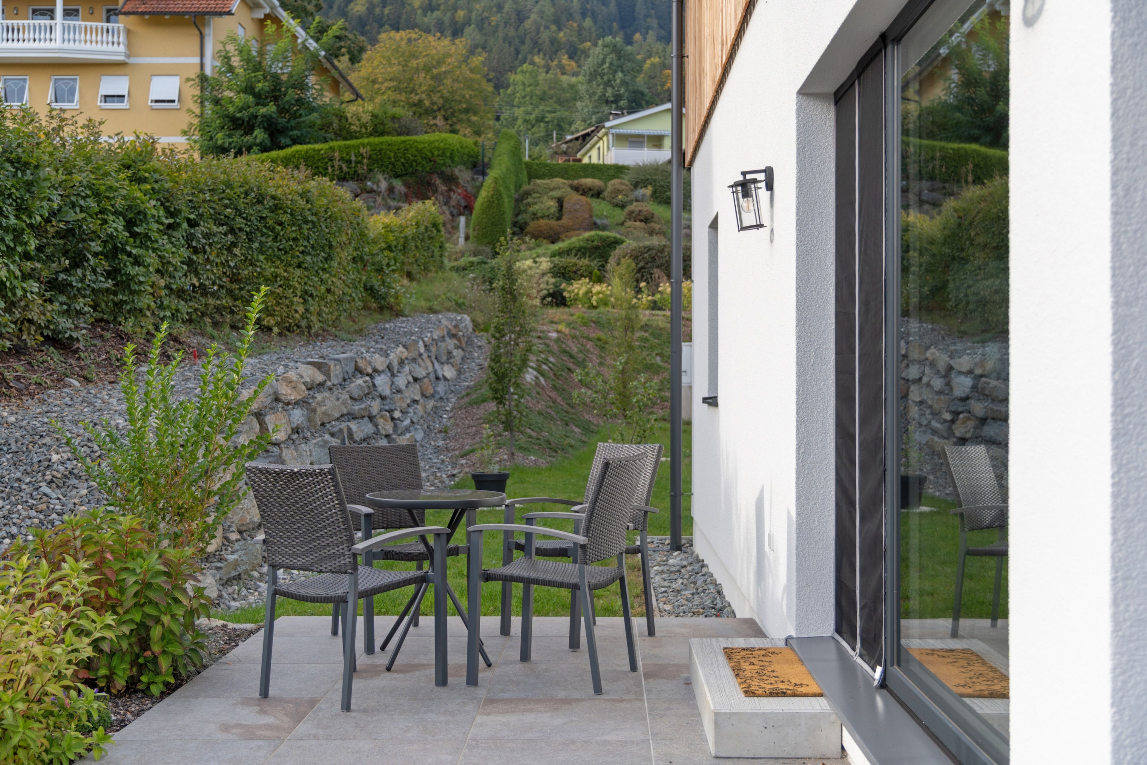An outdoor patio with a table and chairs, a stone wall, and a view of a hillside.