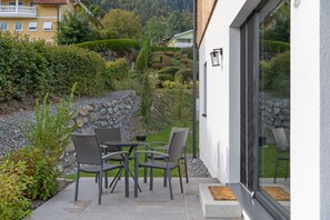 Un patio exterior con mesa y sillas, un muro de piedra y vistas a una colina.