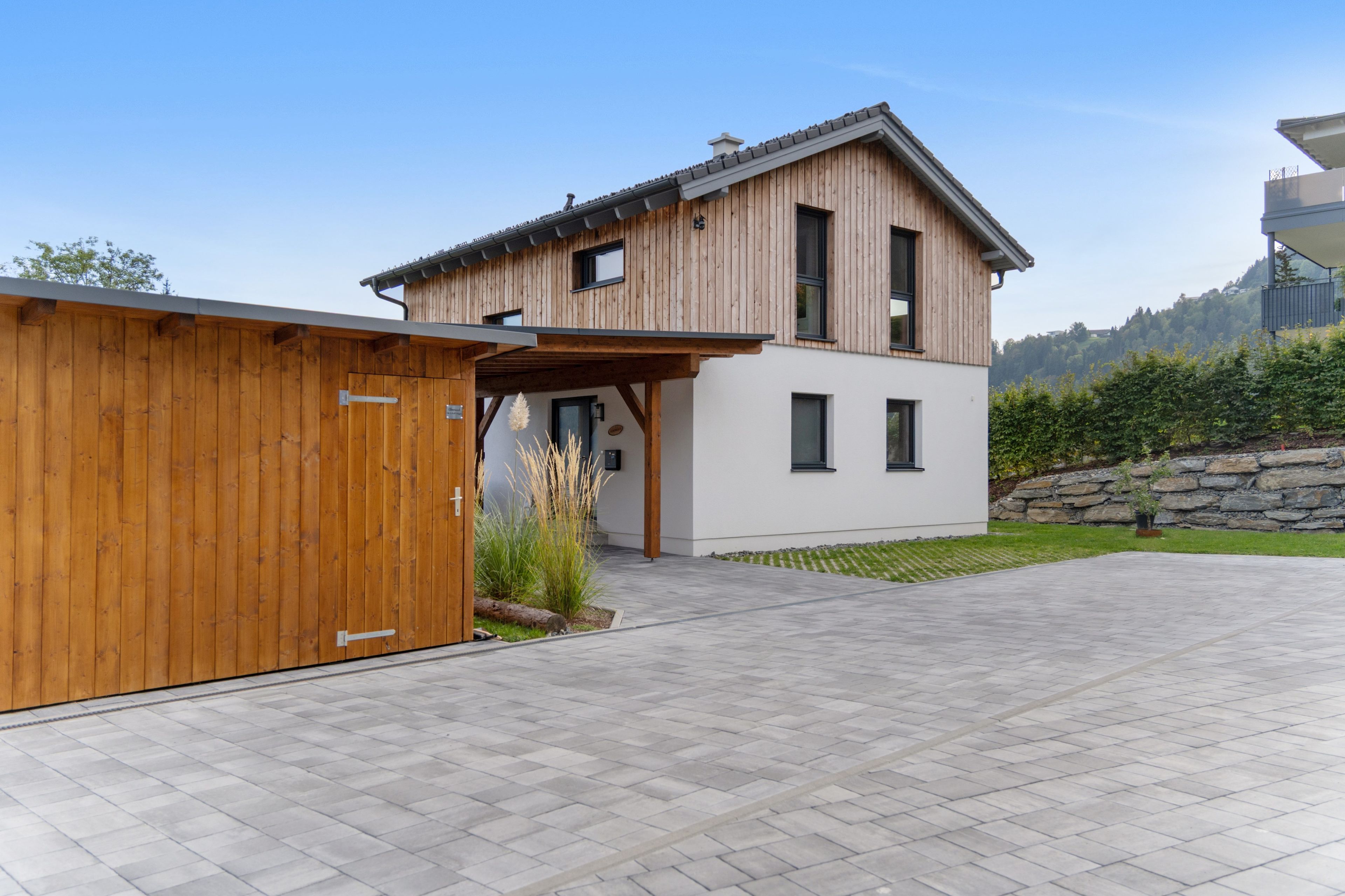 A modern two-story house with a wooden exterior and a stone wall.