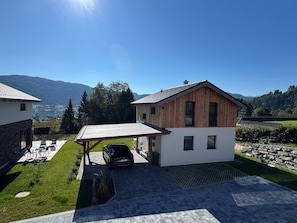 A modern house with a covered patio, a car parked in front, and a view of mountains in the background.