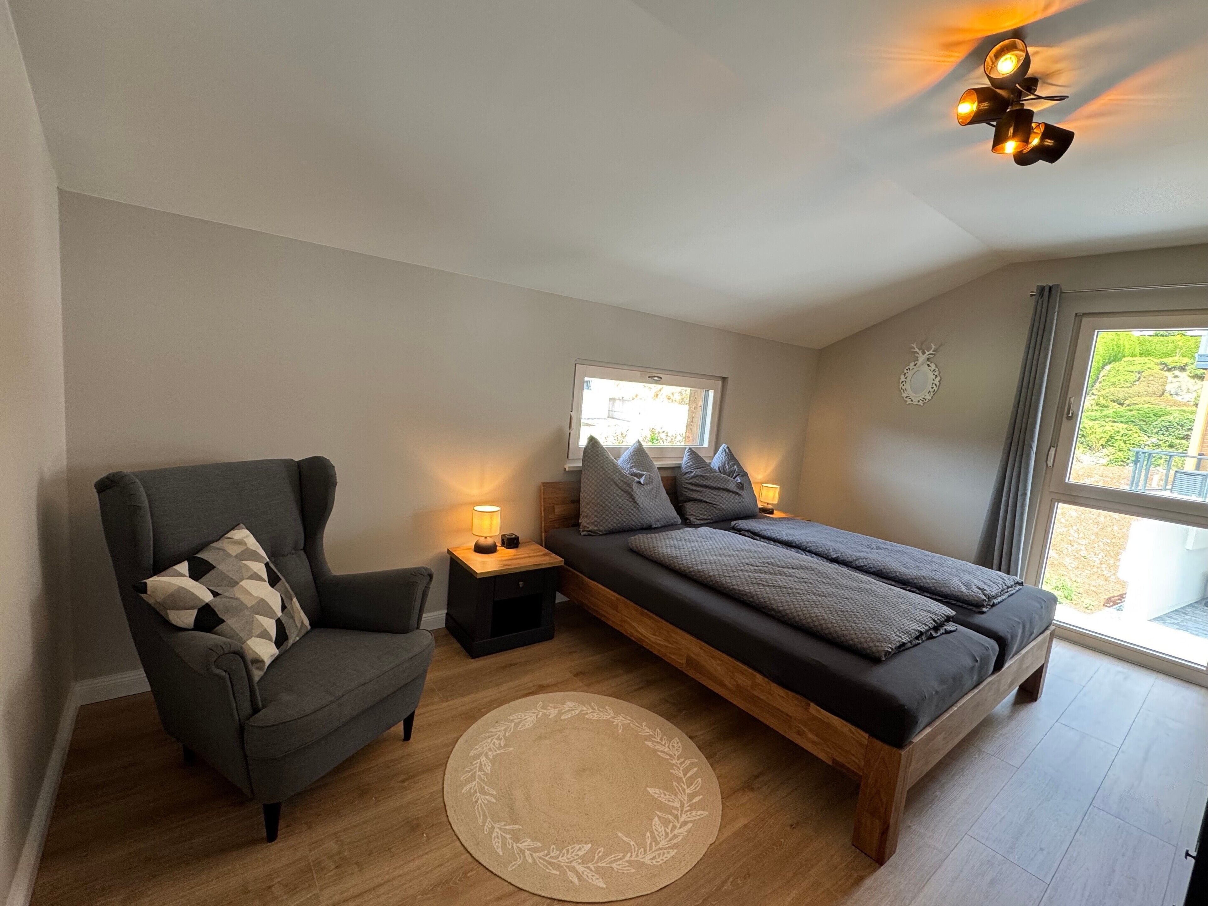 Ein Schlafzimmer mit Bett, Sessel, Nachttisch, Lampe, Deckenventilator und Fenster.
