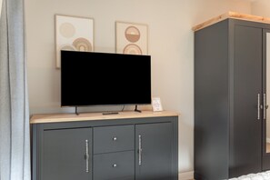 A room with a flat-screen TV on a wooden cabinet, a dark grey wardrobe, and two framed abstract artworks on the wall.