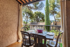 Un balcón con una mesa para dos, sillas, un jarrón grande y vistas a árboles y edificios.