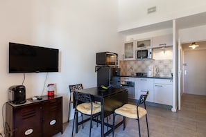Una cocina compacta con microondas, cafetera y televisor montado en la pared.
