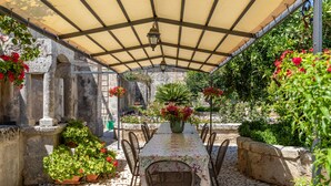 An outdoor patio with a table and chairs, surrounded by potted plants and flowers.