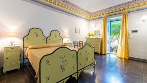 A bedroom with a bed, bedside tables, a dresser, and a window with curtains. - Villa Aguglie - Suite Dalia (Modica)