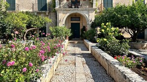 A courtyard with a stone pathway leading to a building with a green door and a balcony with plants. - Villa Aguglie - Suite Dalia (Modica)