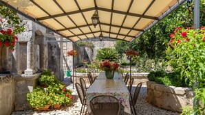 A covered outdoor patio with a table and chairs, surrounded by potted plants and flowers. - Villa Aguglie Suite Gelsomino (Modica)