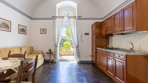 A kitchen with wooden cabinets, a dining area with a table and chairs, and a view through a doorway to an outdoor area. - Villa Aguglie Suite Gelsomino (Modica)