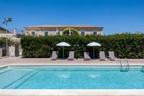 A swimming pool with lounge chairs and umbrellas, a building with a tiled roof, and a clear blue sky. - Villa Aguglie Suite Gelsomino (Modica)