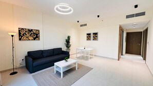 Ein modernes Wohnzimmer mit einem dunklen Sofa, einem weißen Couchtisch und einer kleinen Pflanze. Ein weißer Esstisch mit Stühlen und zwei gerahmte Kunstwerke sind an der Wand zu sehen.