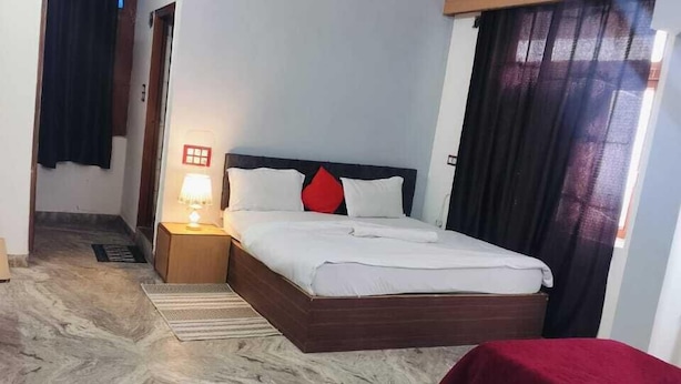 Ein Hotelzimmer mit Bett, Nachttisch mit Lampe, Deckenventilator und Blick durch ein mit Vorhängen versehenes Fenster nach draußen.