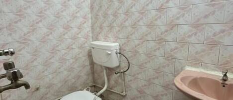 A small, tiled bathroom with a toilet, sink, and trash bin.