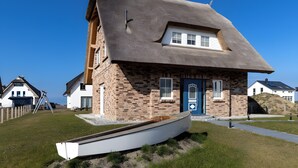 Une maison avec un toit à forte pente, une cheminée bien visible et un petit bateau au premier plan.