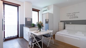 A compact hotel room with a kitchenette, a dining area with a table and chairs, a bed with neatly folded towels, and a motivational quote on the wall. - Italianway Comfort - Bergamo 11 (Milan)